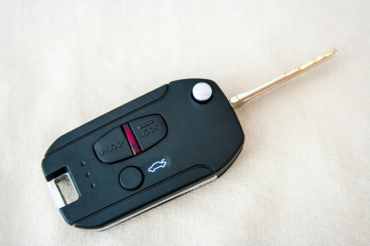 A flip key with lock, open and trunk buttons on a white cloth