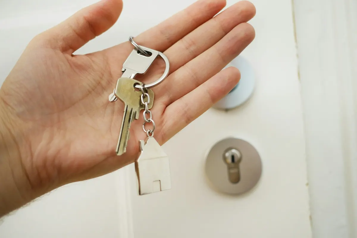 A hand holding a set of house keys next to a deadbolt on a white door